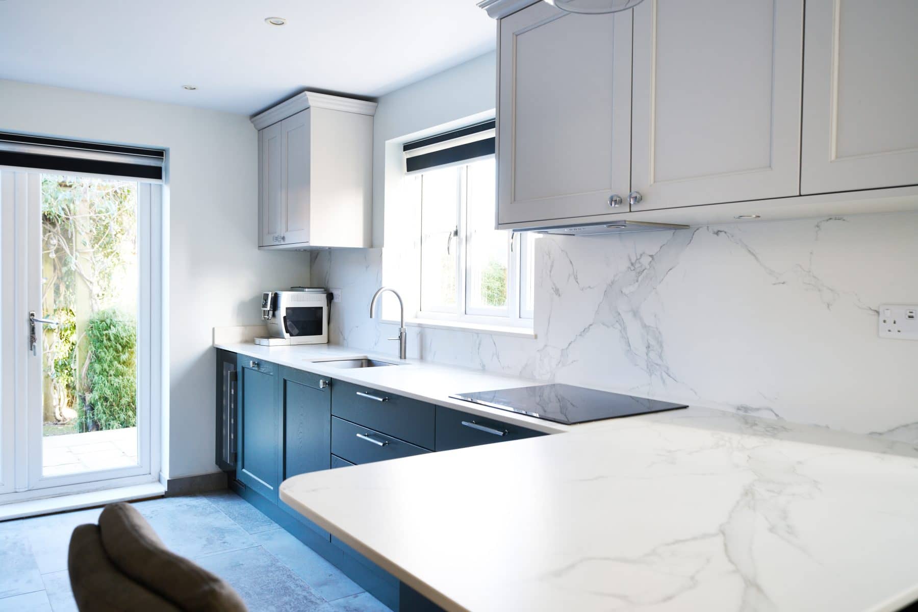 Bright, contemporary kitchen with sleek white and teal shaker cabinetry, white marble countertop and backsplash.