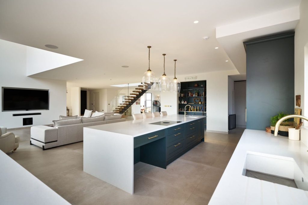 Modern kitchen / lounge space with sleek white counters, a large island with bar stools, and stylish pendant lighting.