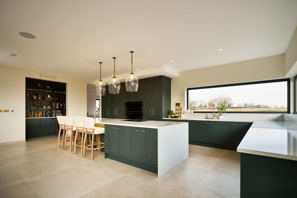 Bright and spacious shaker kitchen featuring a central island, dark green cabinetry, and a large window overlooking the outdoors.