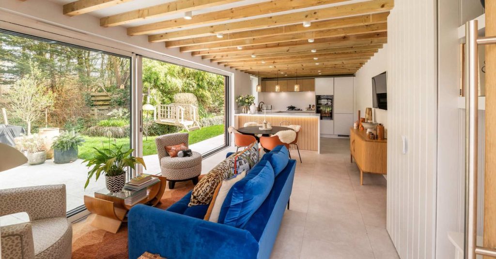 Open plan kitchen with timber beams, blue upholstered sofas and oak acoustic panelling to breakfast bar