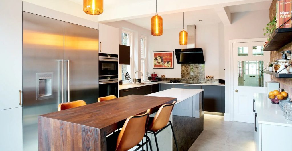 Contemporary german kitchen with amber pendant lights and leather bar stools with island breakfast bar. 