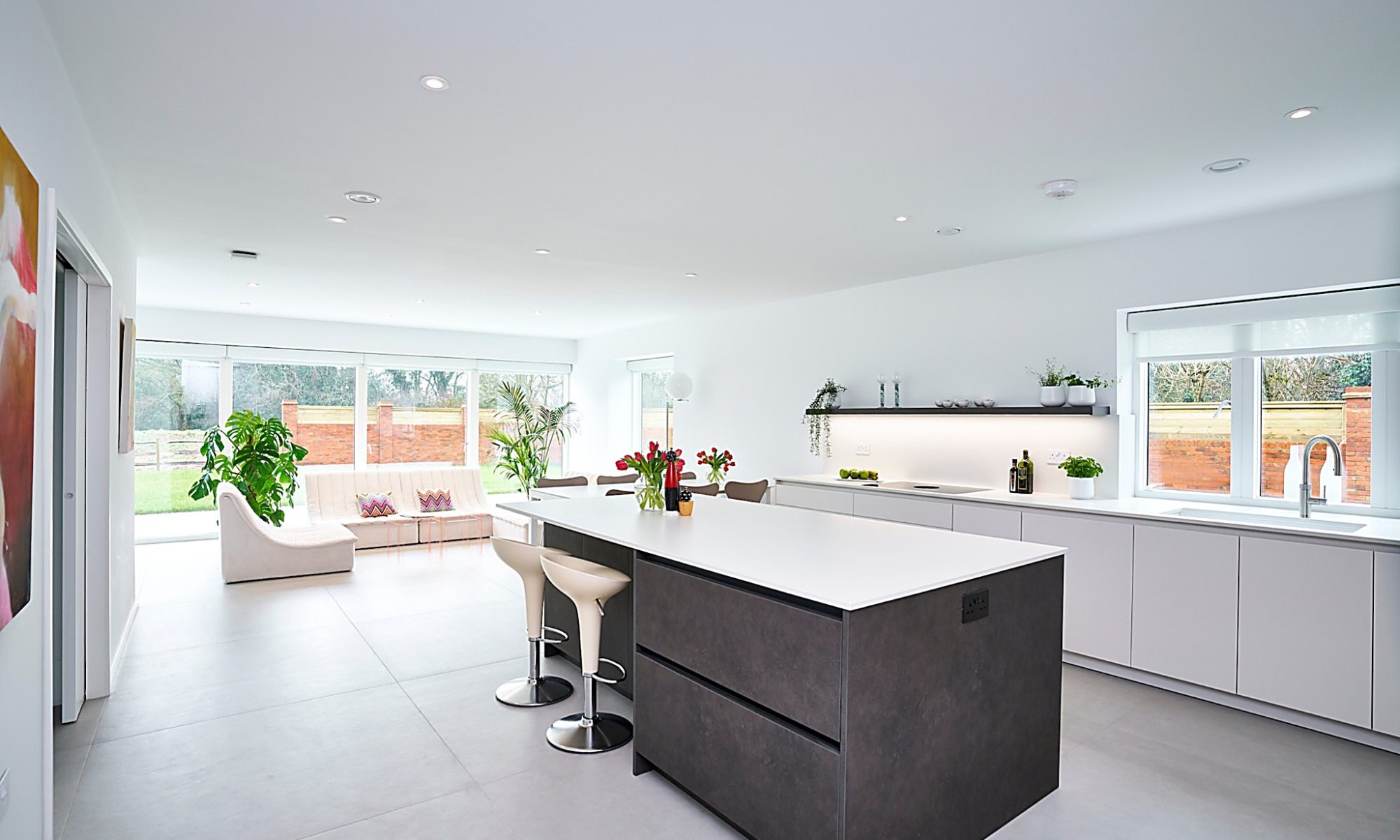 large open plan kitchen with matt white cabinetry, secrete door through into utility and dark grey island