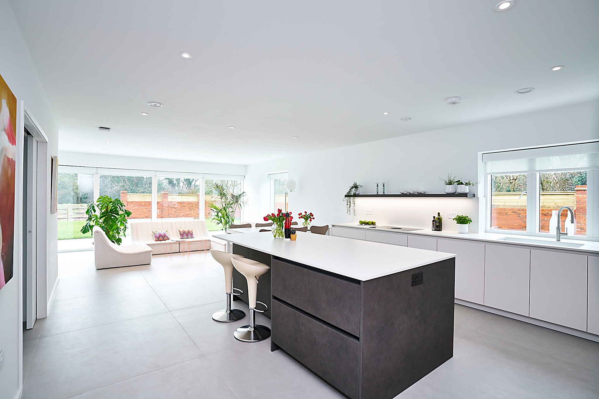 large open plan kitchen with matt white cabinetry, secrete door through into utility and dark grey island