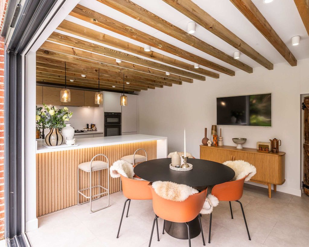 Open plan kitchen diner with slatted wood breakfast bar and orange velvet dining chairs