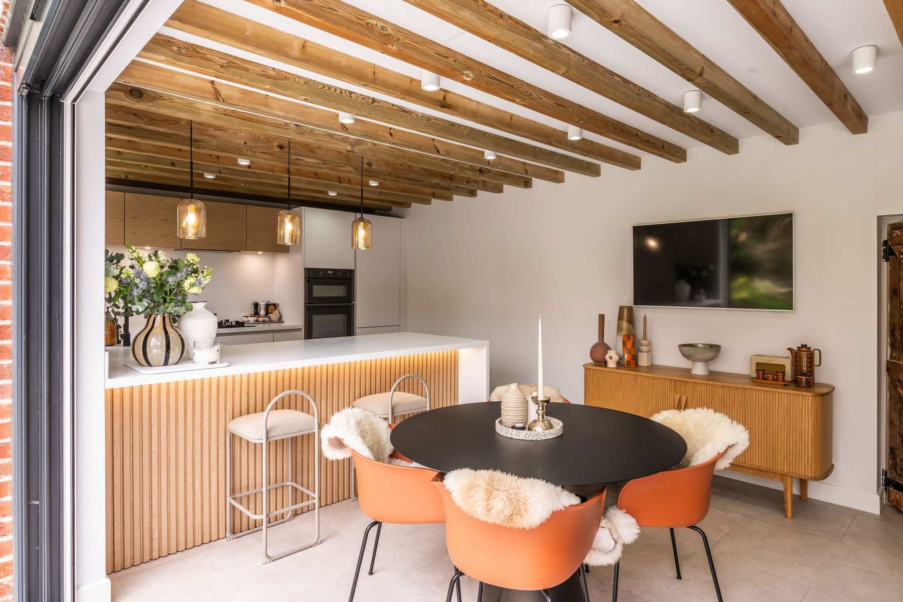 Open plan kitchen diner with slatted wood breakfast bar and orange velvet dining chairs