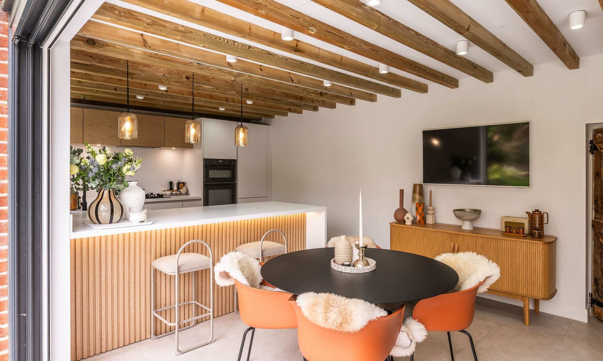 Open plan kitchen diner with slatted wood breakfast bar and orange velvet dining chairs