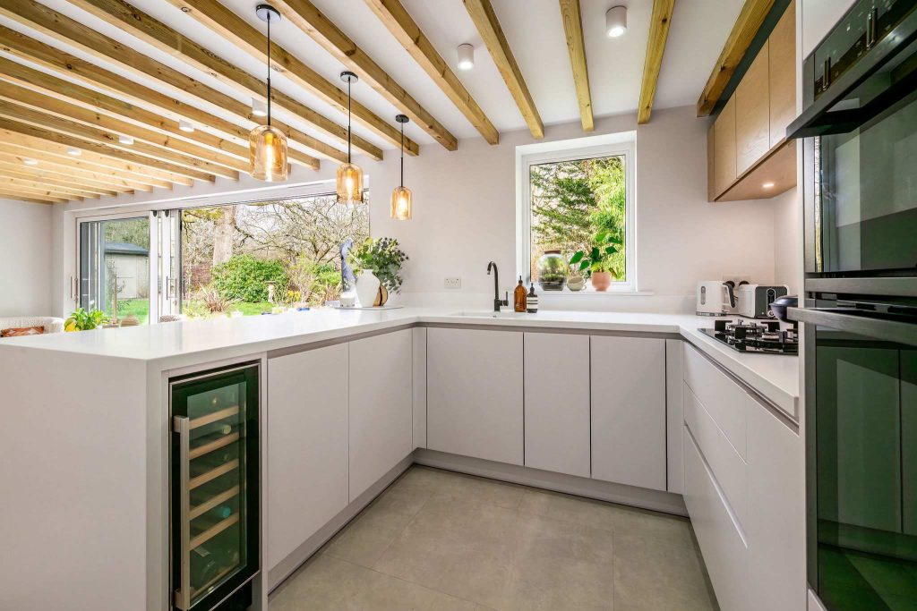 U-shaped handleless kitchen with seamless white worktops and garden view