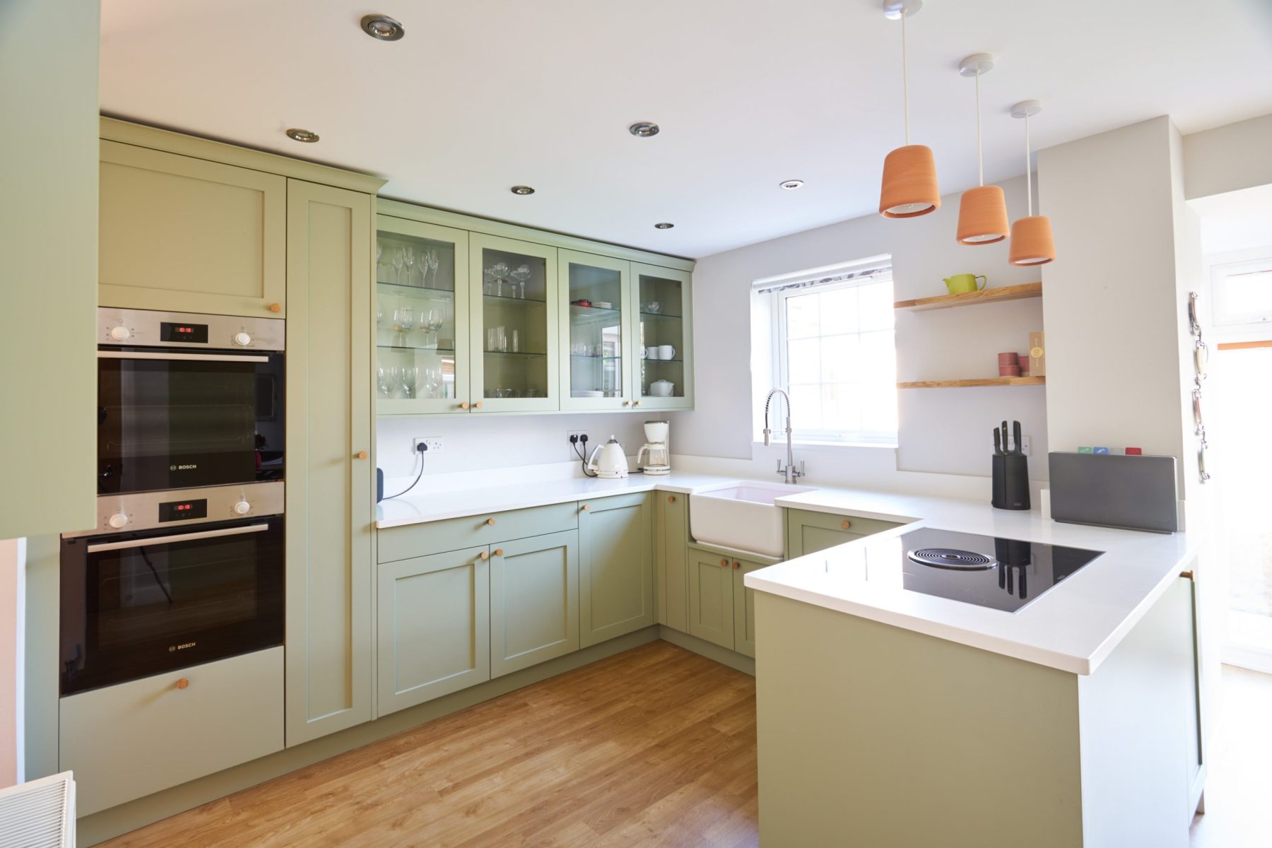 Soft green u shaped shaker kitchen cabinets with open shelving and glass wall cabinets