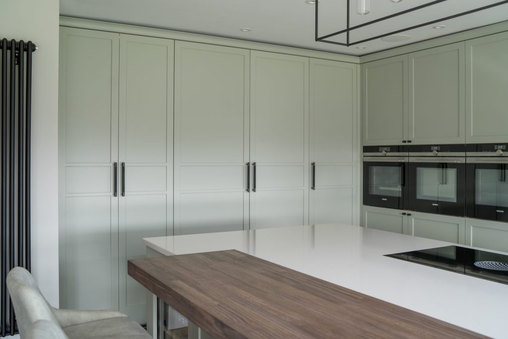 Pale green tall shaker larder units with kitchen island, additional dark wood bar
