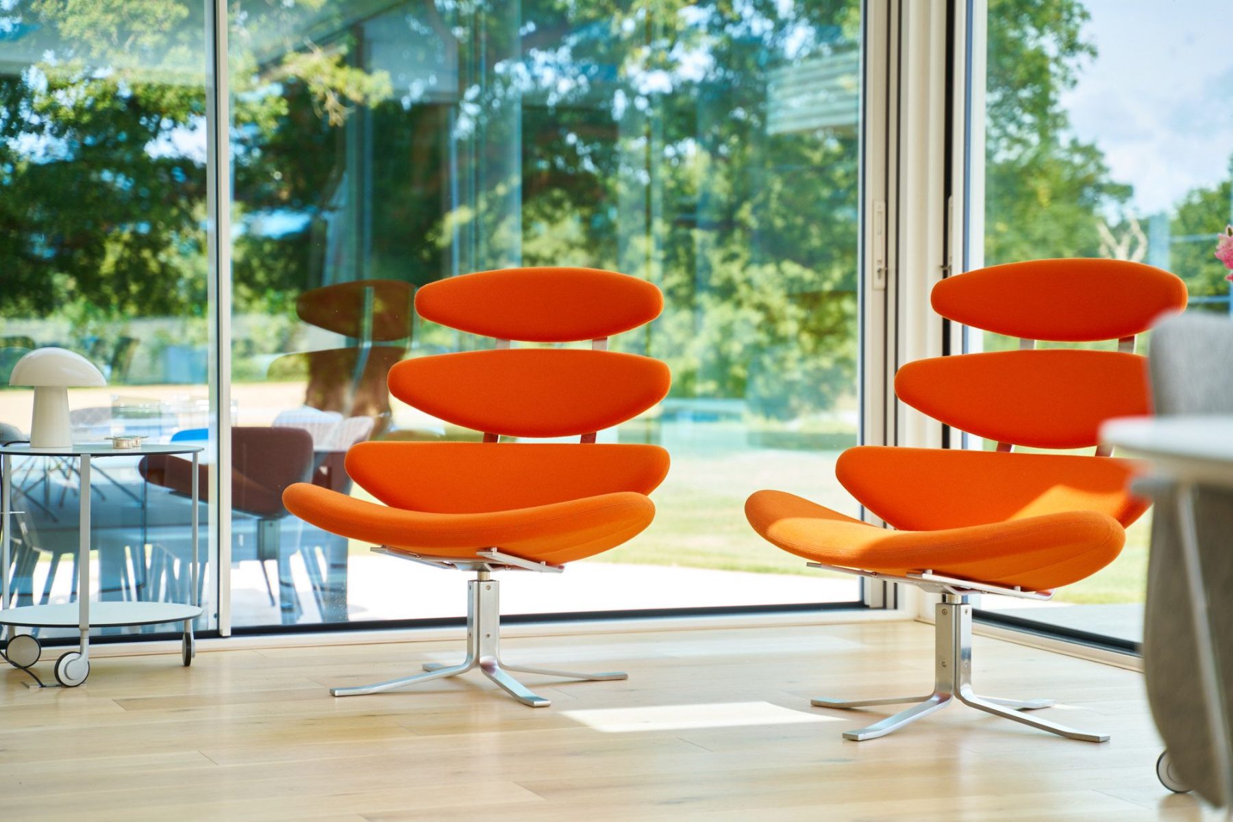 Pair of contemporary orange lounge chairs in a bright glass-walled living space with panoramic garden views.