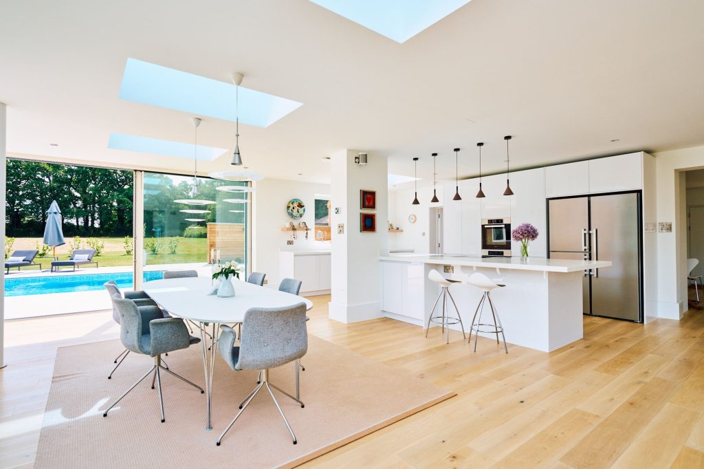 Luxury open-plan kitchen and dining area with pool view, white cabinetry, skylights, and modern pendant lights.