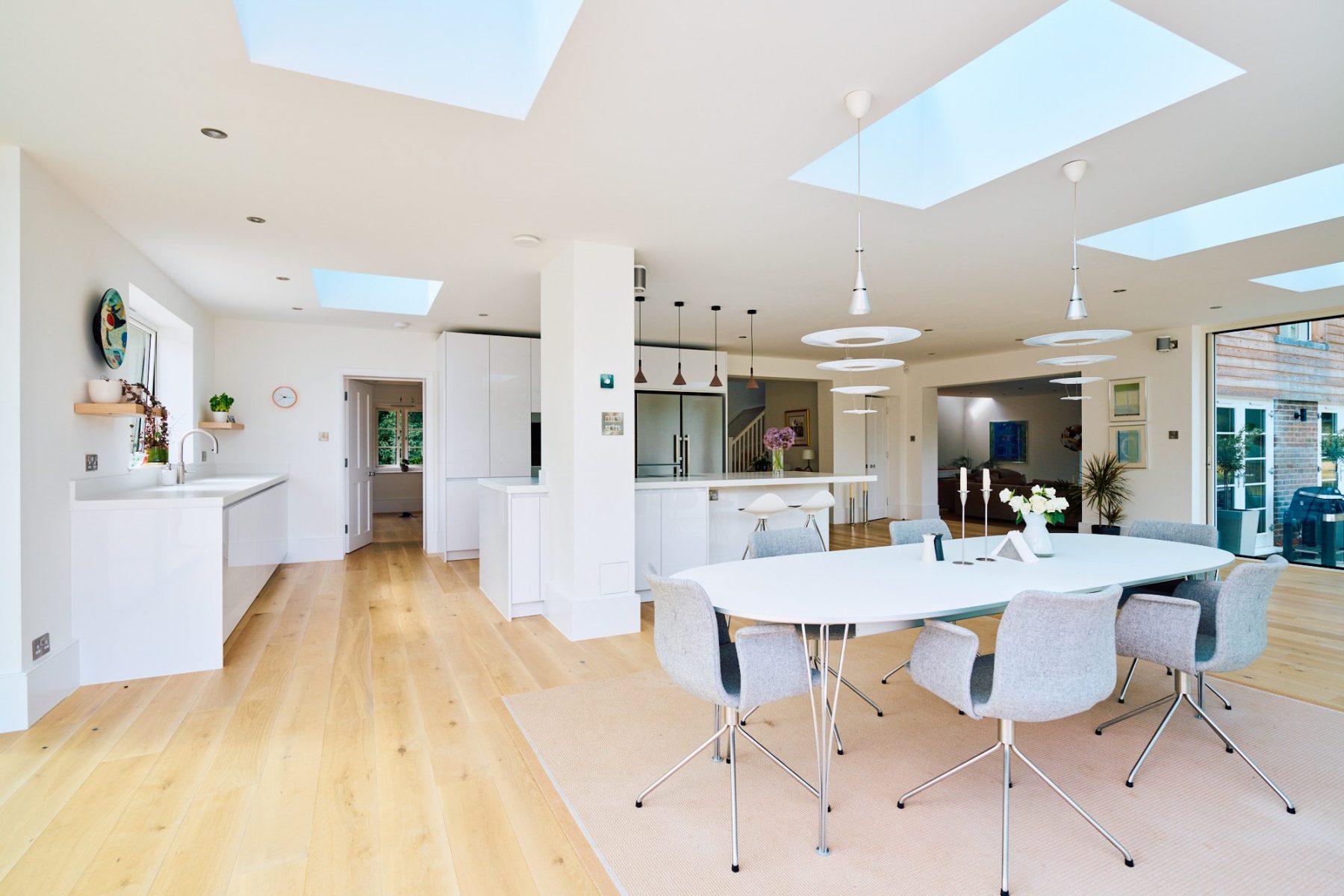 Light-filled open-plan kitchen with skylights, dining area, and white gloss cabinetry in a modern home.
