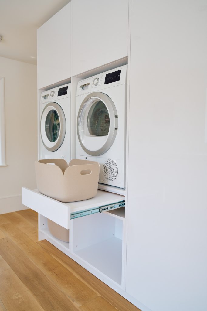 Bespoke utility room with pull-out laundry platform, stacked washing machine and dryer, and integrated storage.