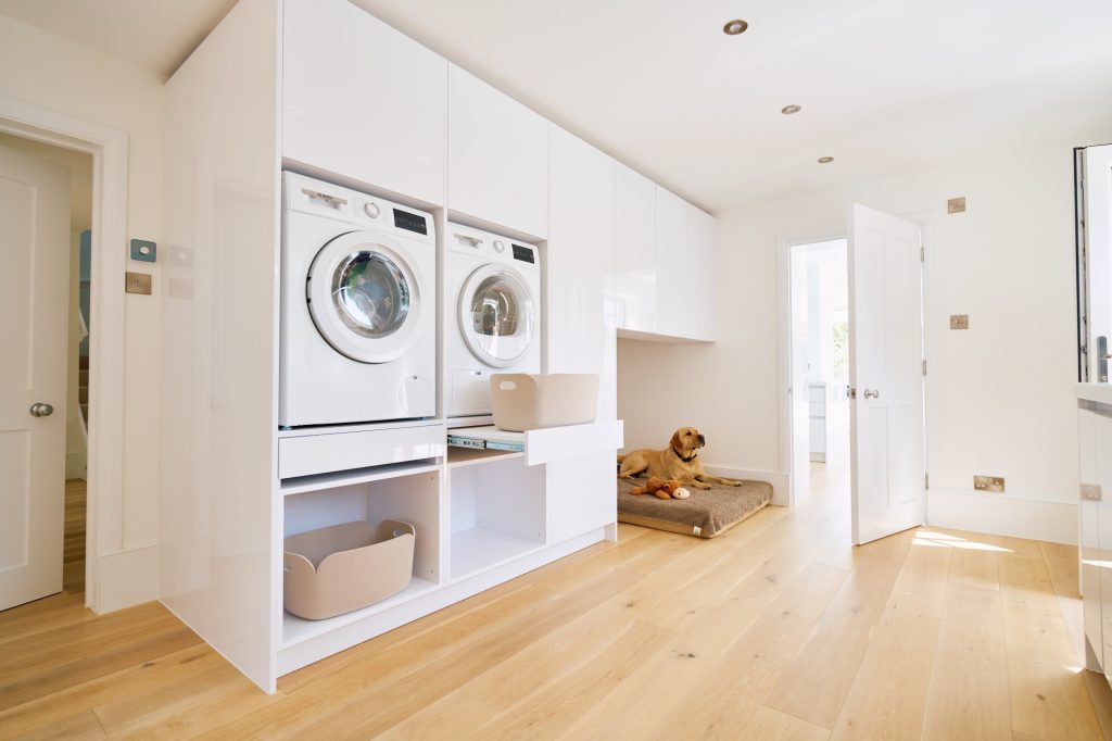 Contemporary utility room with stacked laundry appliances, dog bed space, and glossy white cabinetry.