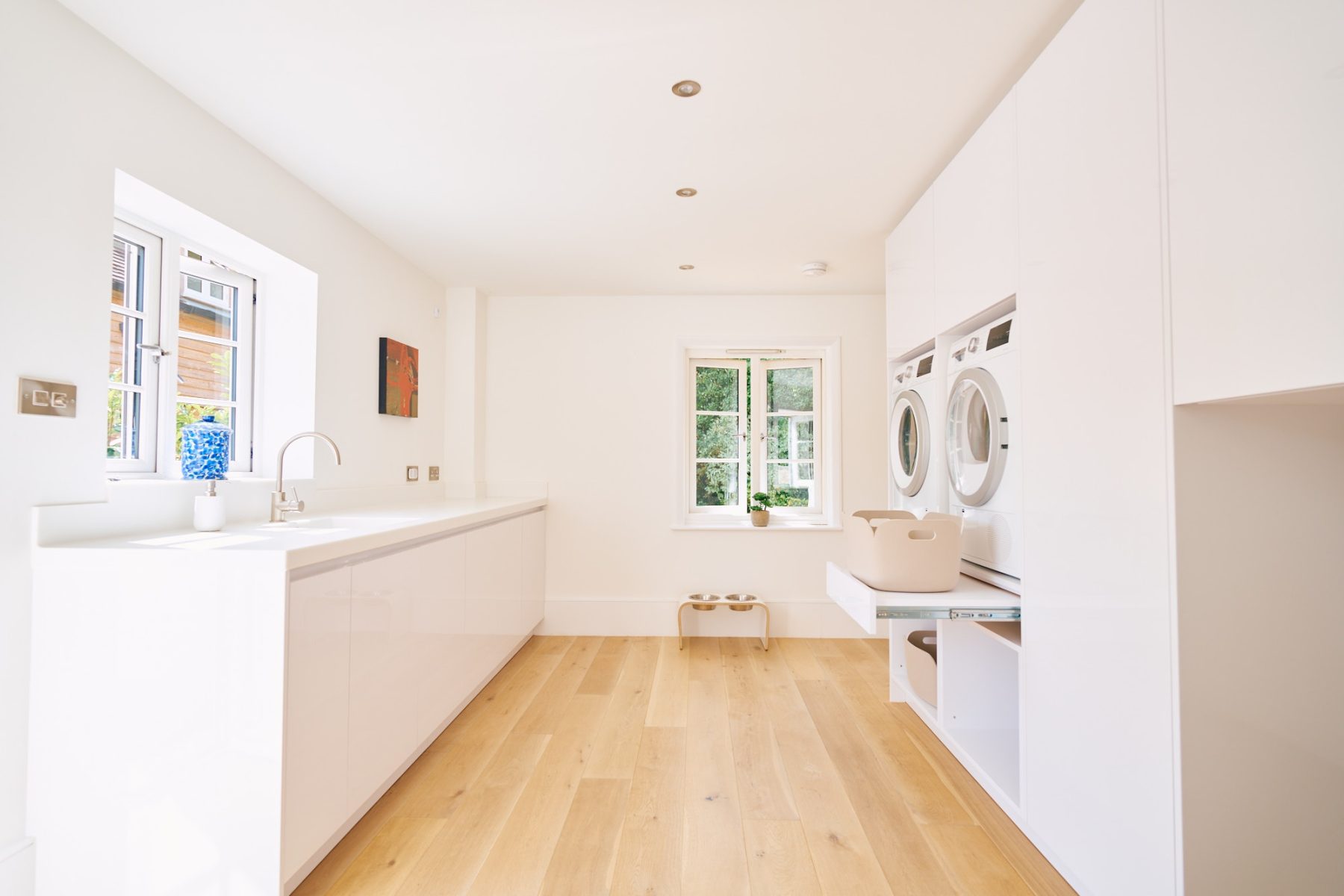 Minimalist utility room with white gloss cabinetry, oak flooring, and large countertop workspace.